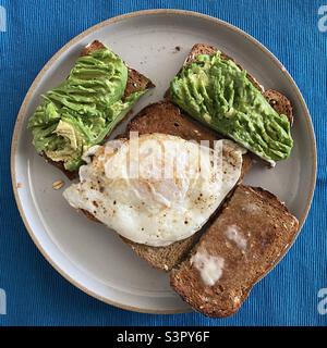 Breakfast with whole grain avocado toast and a fried egg on a grey ceramic plate Stock Photo