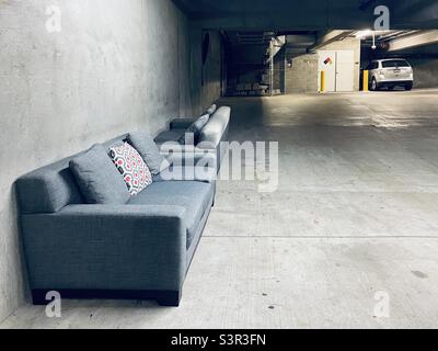 Two grey couches with cushions, left on cement floor at the side of a a basement parking garage Stock Photo