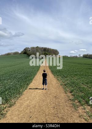 Disappearing perspective, boy on path through field on hill. Stock Photo