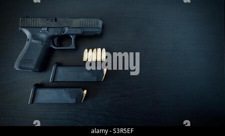 Hand gun with two fully loaded magazines and 9 mm brass ammo on dark wooden table, copy space Stock Photo