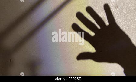 Shadow of a hand on a white textured surface, with colored diffraction pattern from a light source with a lens Stock Photo