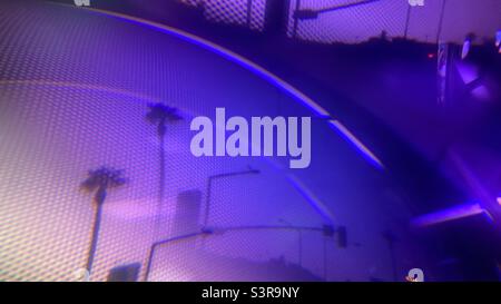 Purple abstract background created with prism in front of camera lens. Street lights and palm trees seen through meshwork, focus on foreground Stock Photo