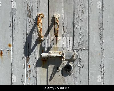 Old wooden door with peeling white paint, rusting handles and bolt. Stock Photo