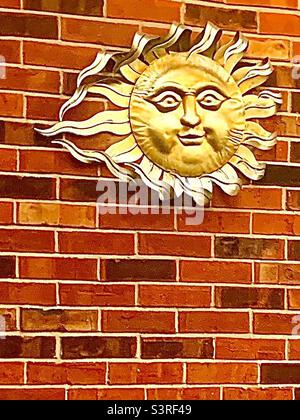 Smiling golden sun accessory in top corner of red brick wall Stock Photo