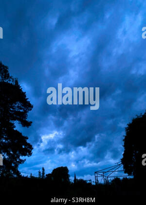 A moody, cloudy sky during the blue hour in the evening with a garden in silhouette. Stock Photo