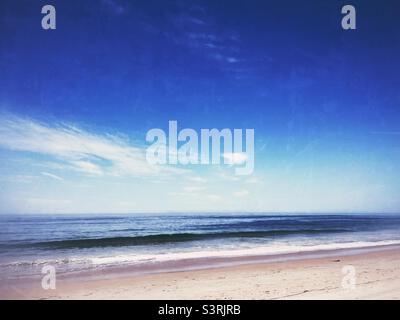 Sandy beach with ocean waves rolling onto shore on a sunny day. Stock Photo