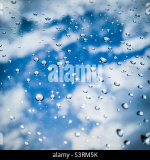 Water droplets on a window with clods and a blue sky background Stock Photo