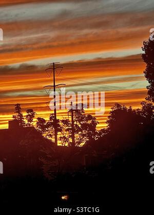 Summer sunset from a homes’ upstairs window in Utah, USA. The local Utah neighborhood is seen in silhouette against a radiant, glowing sky. Stock Photo