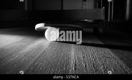 Shallow focus black and white view with dramatic lighting of a ping pong or table tennis ball and bat resting on a worn table Stock Photo