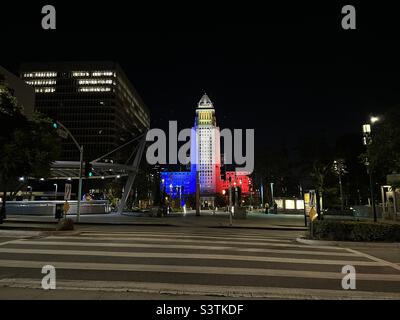 LOS ANGELES, CA, OCT 2021: wide view of City Hall in Downtown at night, with blue, white and red lighting on the building. Pedestrian crossing and LA Metro subway station in foreground Stock Photo