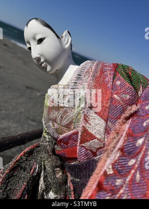 Close up of a broken Japanese doll in kimono on a beach Stock Photo