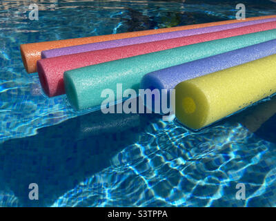 Rainbow coloured pool noodles floating in sparkling water of swimming pool. Stock Photo