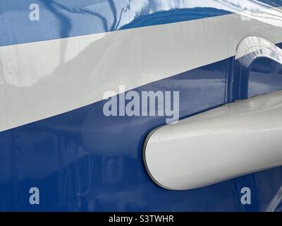 Close up view of fuselage of passenger aircraft exterior, light blue and dark blue stripes on white with reflections. Suitable for background for graphics and text Stock Photo