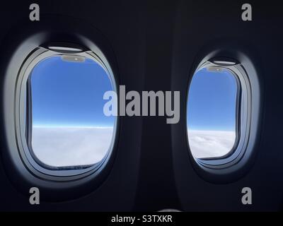 Looking through silhouetted airplane windows at white, fluffy clouds below and deep indigo sky overhead Stock Photo