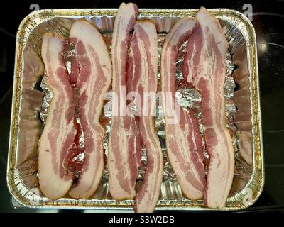 Raw strips of bacon in aluminum foil tray about to go into oven for cooking Stock Photo