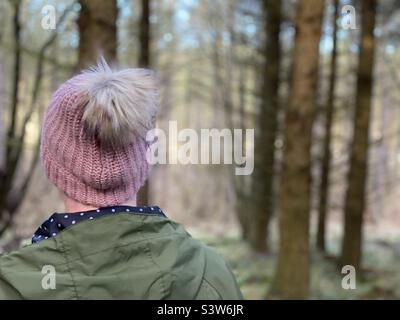 Rear view of woman wearing a knit hat walking in woodlands Stock Photo