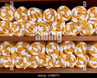 White and yellow towels rolled up and waiting by the poolside on board a cruise ship Stock Photo