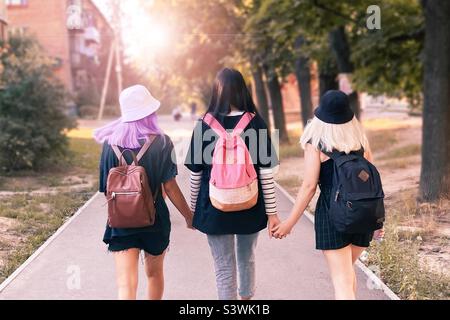 Three teenagers students walking together with backpacks by the city street Stock Photo