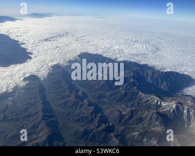 View from aircraft flying over mountains with a blanket clouds covering scenery below Stock Photo