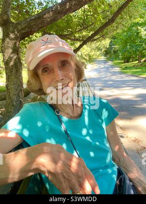 A smiling senior woman sits under the trees in Central Park, New York City, USA Stock Photo