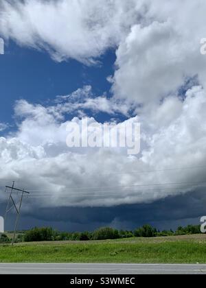 A summer storm passing by across the field. Blue sky above clouds, fluffy white on top and heavy and dark below, rain streams down in the distance. Stock Photo