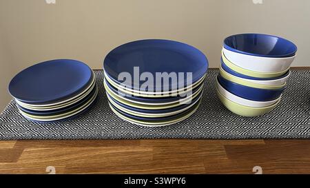 Set of blue, green, and white ceramic plates, dinner plates, and bowls on a wooden table with patterned cloth Stock Photo