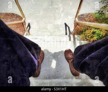 Man in Sunday dress sitting on outdoor steps at a local church in Utah, USA. Casually relaxing on a sunny day, image is shot while sitting looking down the steps between the man’s knees-Perspective! Stock Photo