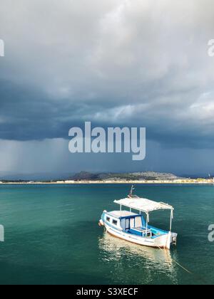 A boat in sun in the sea at Nafplio, Greece, with dark stormy clouds on the horizon Stock Photo
