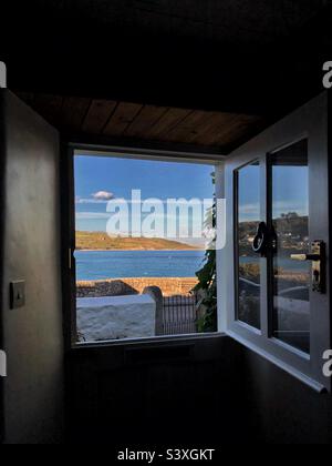 A view through a half barn door of a quaint coastal cottage onto a seascape vista with copy space Stock Photo
