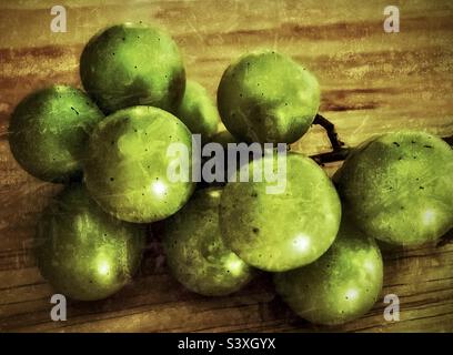 A small bunch of fresh green grapes placed upon a wooden kitchen table. Lighting and grunge effects applied using the IOS app Snapseed. Stock Photo