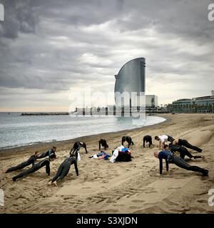 A school of surfing school students warmup for their morning lesson on the busy city beach of Barceloneta in front of the W Barcelona Hotel in Barcelona, Spain Stock Photo