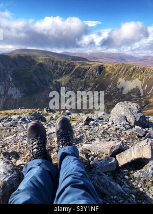 View of Walkers feet and leather boots on the Rocky slopes of the Cairnwell at Glenshee with a view towards The ridge of Creag a’ Choire Dhirich, Scotland Stock Photo