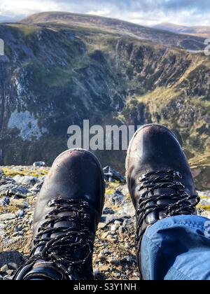 View of Walkers feet and leather boots on the Rocky slopes of the Cairnwell at Glenshee with a view towards The ridge of Creag a’ Choire Dhirich, Scotland Stock Photo