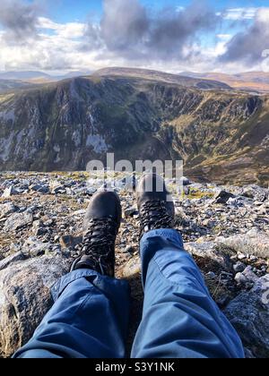 View of Walkers feet and leather boots on the Rocky slopes of the Cairnwell at Glenshee with a view towards The ridge of Creag a’ Choire Dhirich, Scotland Stock Photo