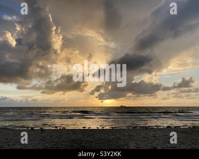 at the sea the red-golden sun shines out from behind the clouds before it sets Stock Photo