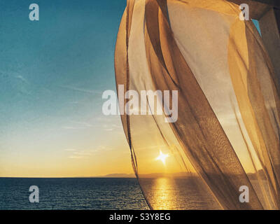 Sunset over Lardos Bay from Pefkos on Rhodes viewed through fluttering curtain Stock Photo
