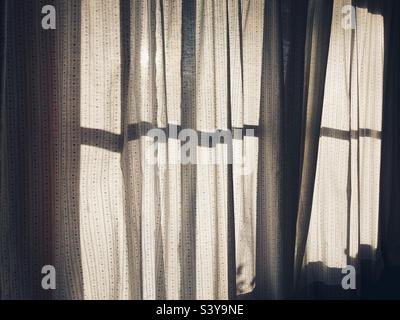 Sheer Curtains with sunlight shining through the lattice window behind them Stock Photo