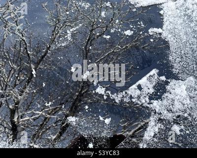 Fresh snow and ice have been scraped from an SUV’s windshield after heavy snowfall occurred overnight in this Utah, USA neighborhood. Cool abstraction made from reflections in glass & snow particles. Stock Photo