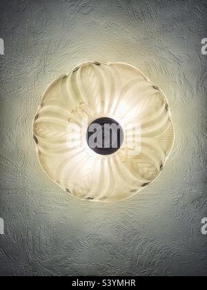 Shot directly from below, this decorative glass light fixture emits a soft, warm glow and creates a central symmetrical design while also bringing out the ceiling texture. Stock Photo