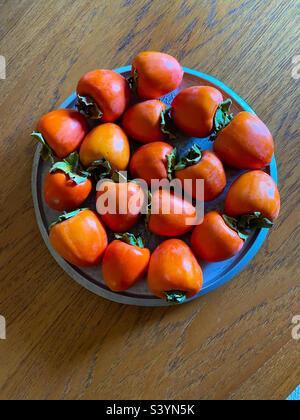 A tray of ripe persimmons on a wooden table Stock Photo