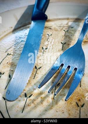 A knife and fork lay on a dirty empty plate Stock Photo