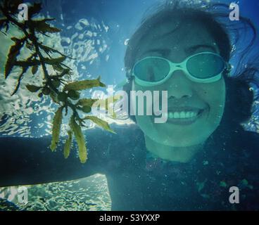 A woman under the water smiling wearing speedo googles and rash guard. Snorkeling in Bahamas. Stock Photo