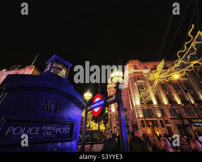 Old London police box in Piccadilly Circus with London Underground Roundel - Christmas lights and decorations across the street - London at night Stock Photo