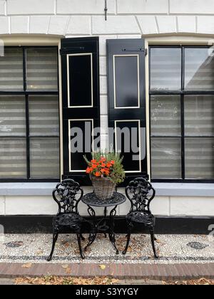 Table and chairs with red flowers outside a shuttered building in Elburg, Netherlands. Stock Photo