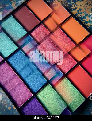 A vibrant palette of colourful eyeshadows and lipgloss against a patterned background and shot through a kaleidoscopic lens Stock Photo