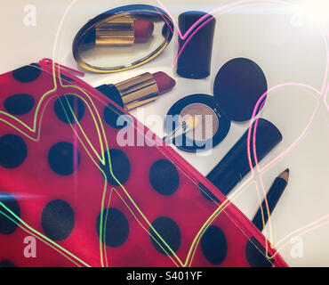 An unbranded selection of cosmetics in black cases spilling out of a red & black polka dot bag, with heart overlay Stock Photo