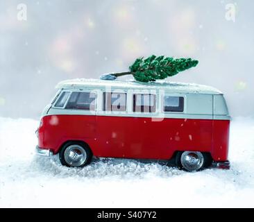 Red toy camper drives through a snowy scene with a Christmas tree on its roof Stock Photo