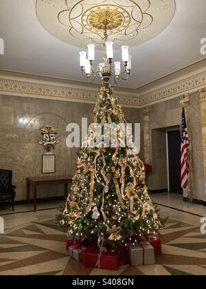 Festive Christmas tree with ribbons at Clinton, Connecticut town hall. Under the tree are red and silver presents. And behind is a US flag and table. Stock Photo
