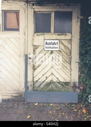 Old wooden door with sign with German text: Ausfahrt freihalten which translates into Keep the exit clear in English language Stock Photo