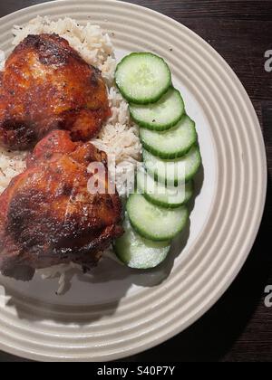 Sweet BBQ chicken on a bed of rice served with sliced cucumber. Stock Photo